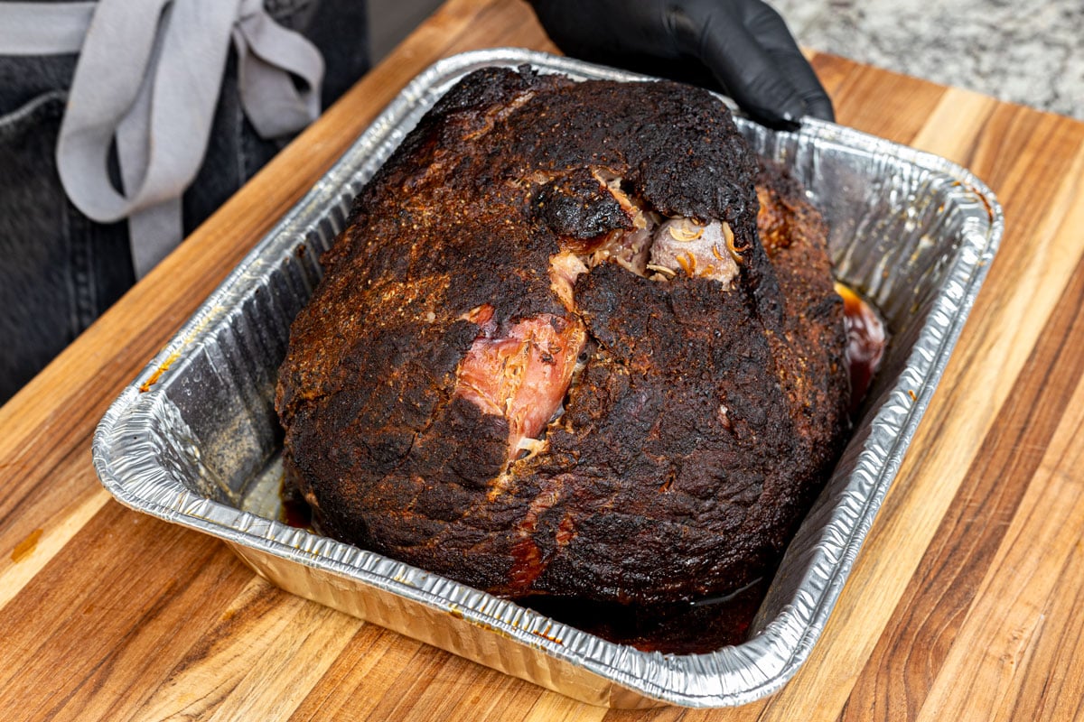 Smoked ham is resting in a foil pan before shredding.