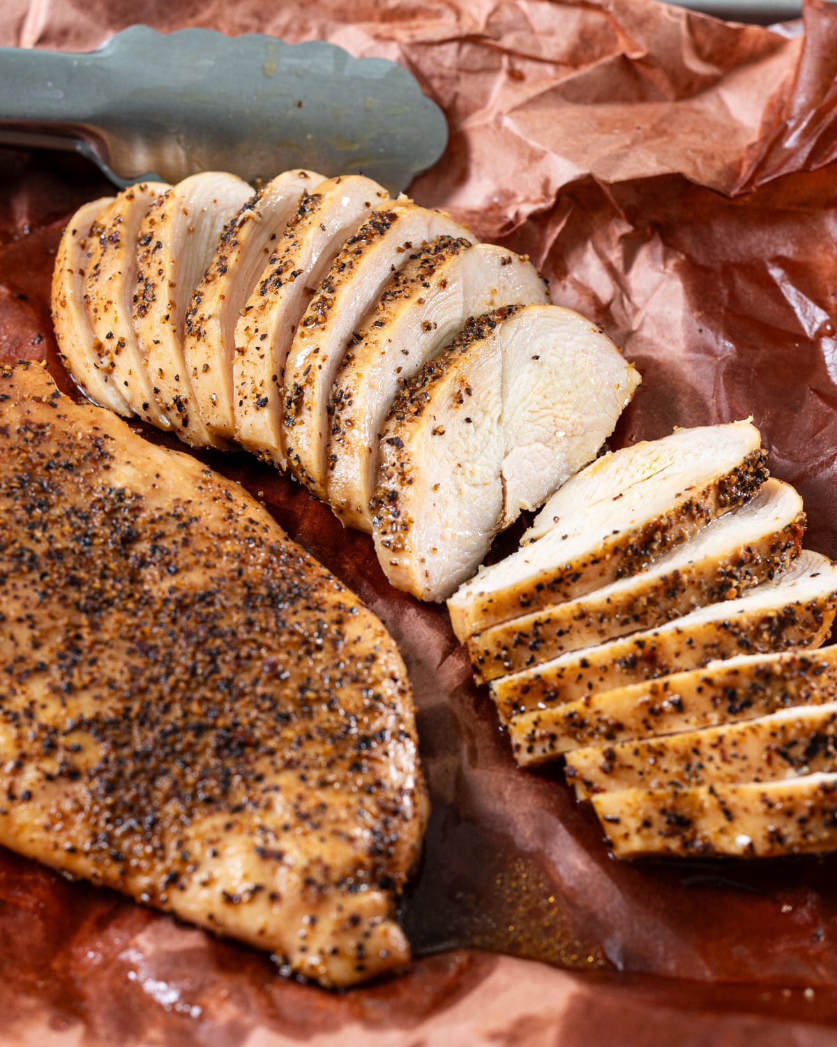 Sliced smoked chicken breast on pink butcher paper next to a whole breast.