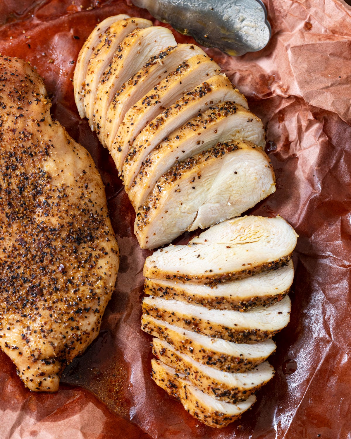 Overhead shot of a seasoned and sliced chicken breast on pink butcher paper.
