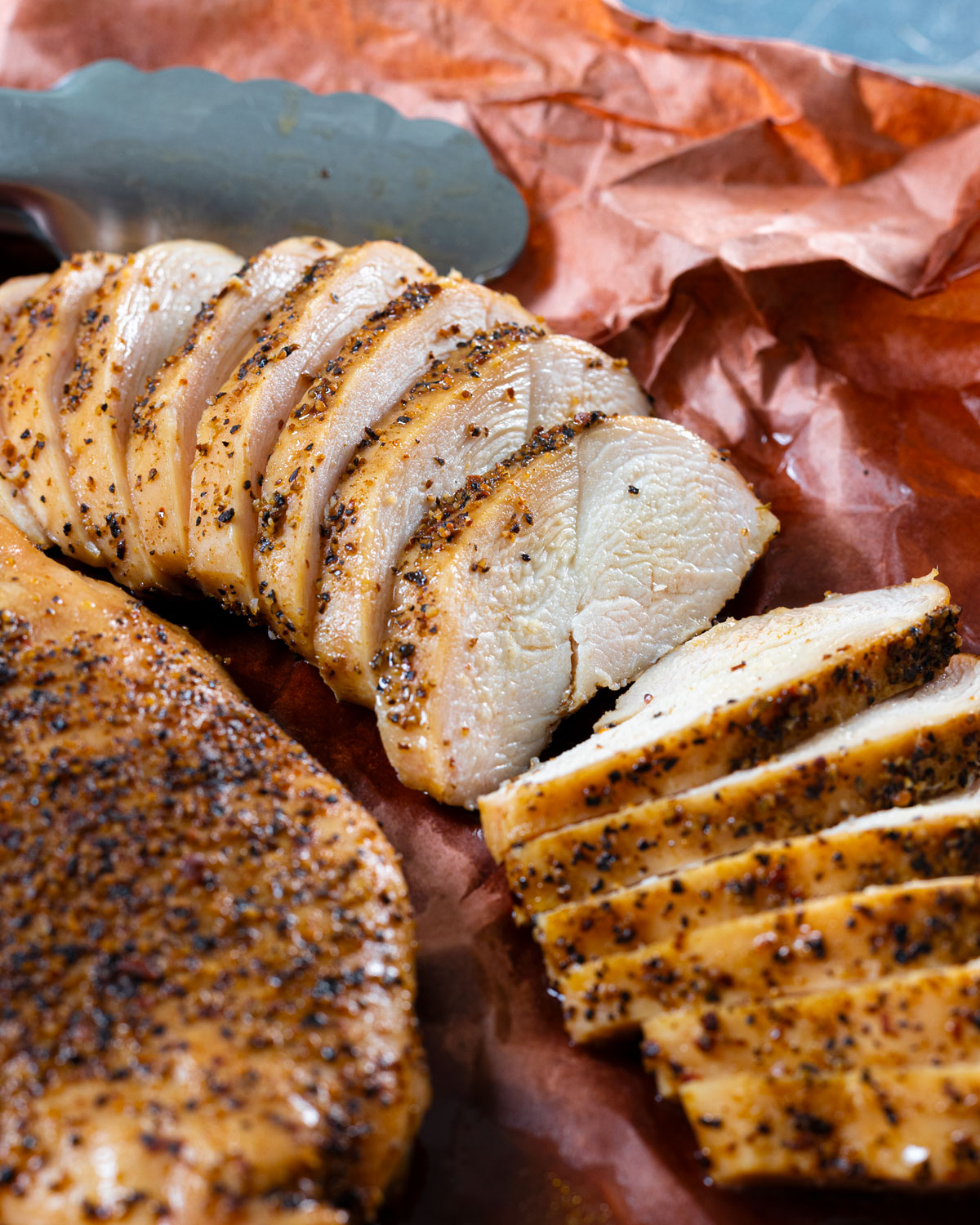 Juicy smoked chicken breast sliced and placed on pink butcher paper.