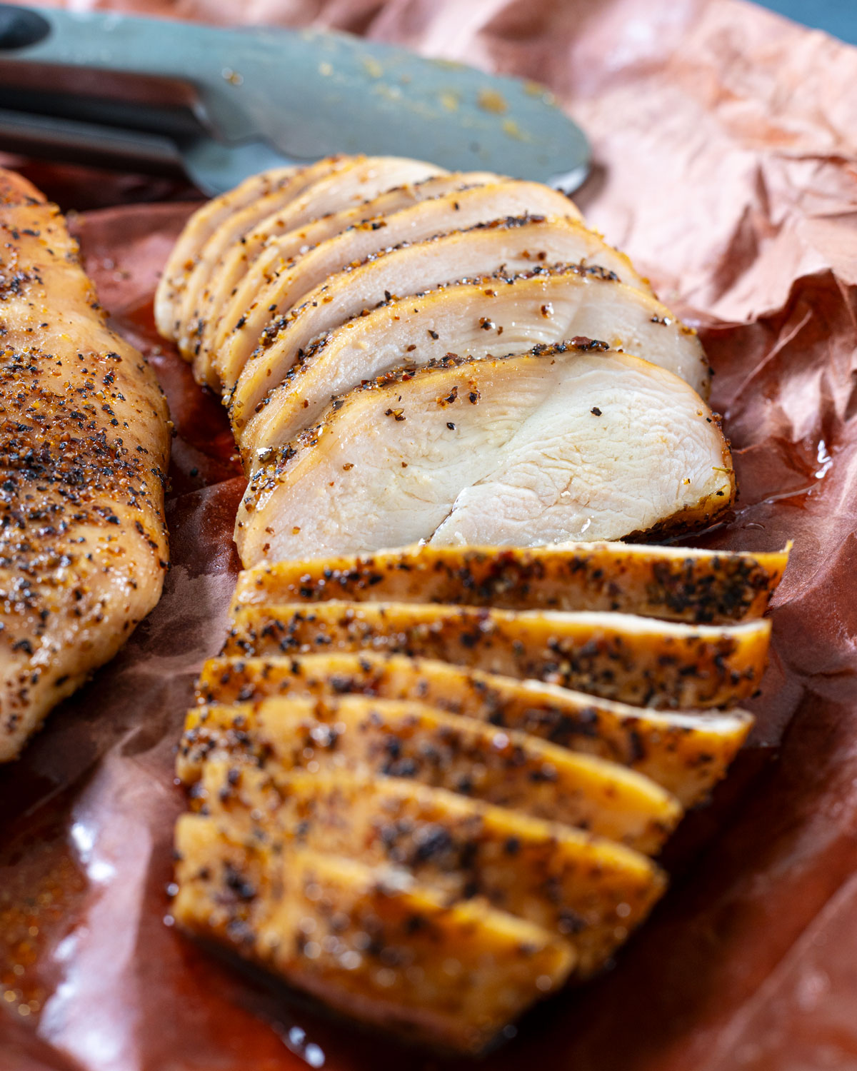 Sliced smoked chicken breasts on pink butcher paper, showing the juicy inside.
