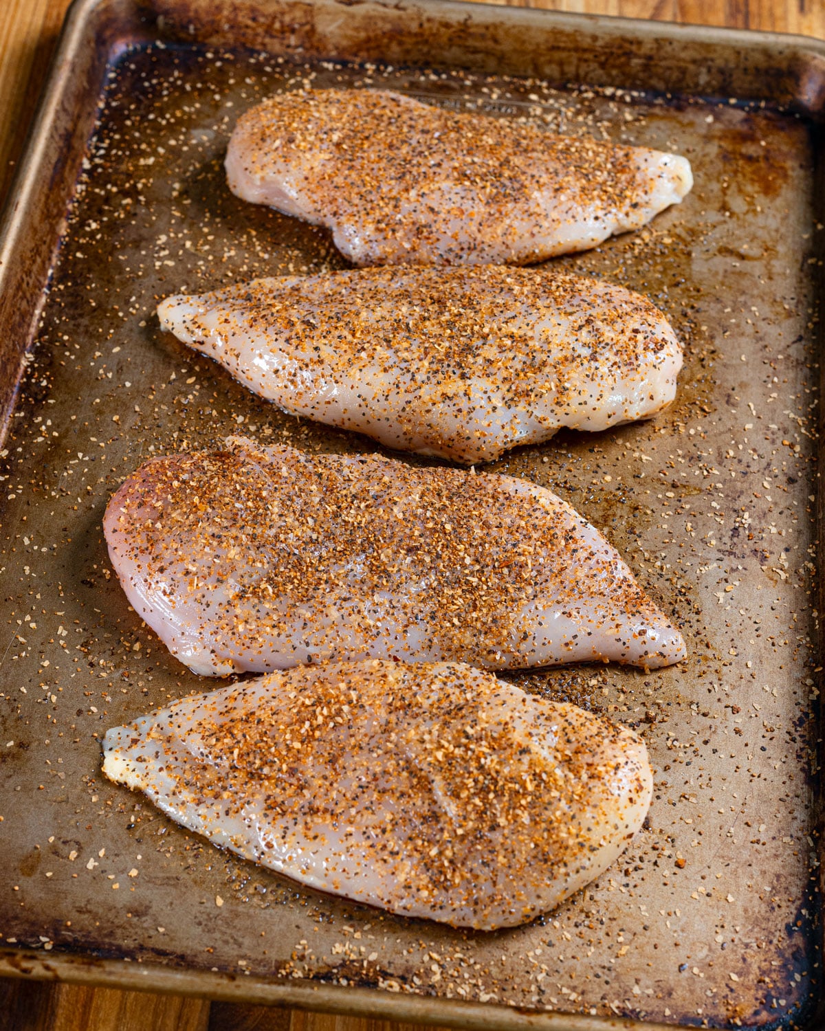Four chicken breasts seasoned on a sheet pan.
