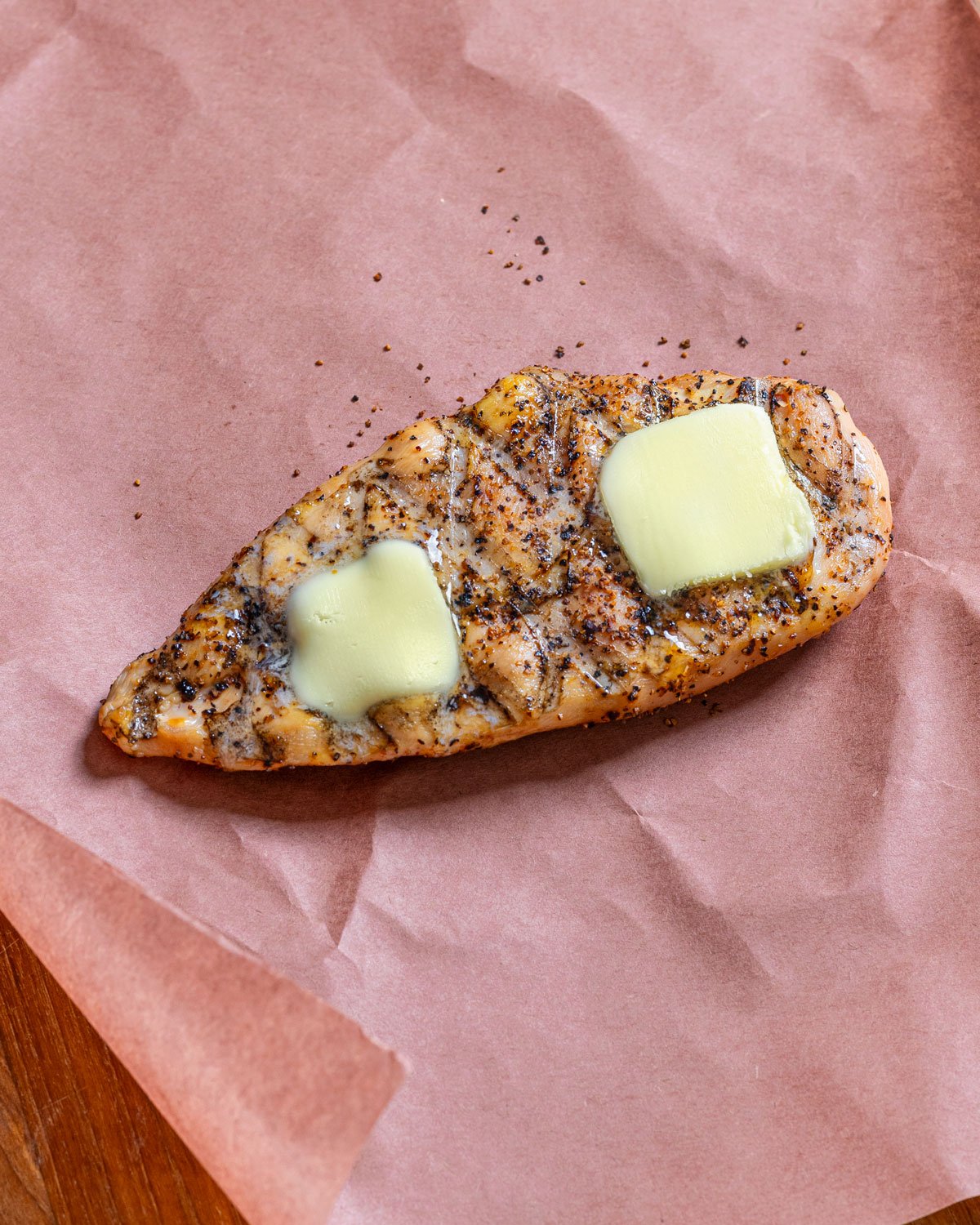 Butter placed on top of smoked chicken breast on a piece pf pink butcher paper.