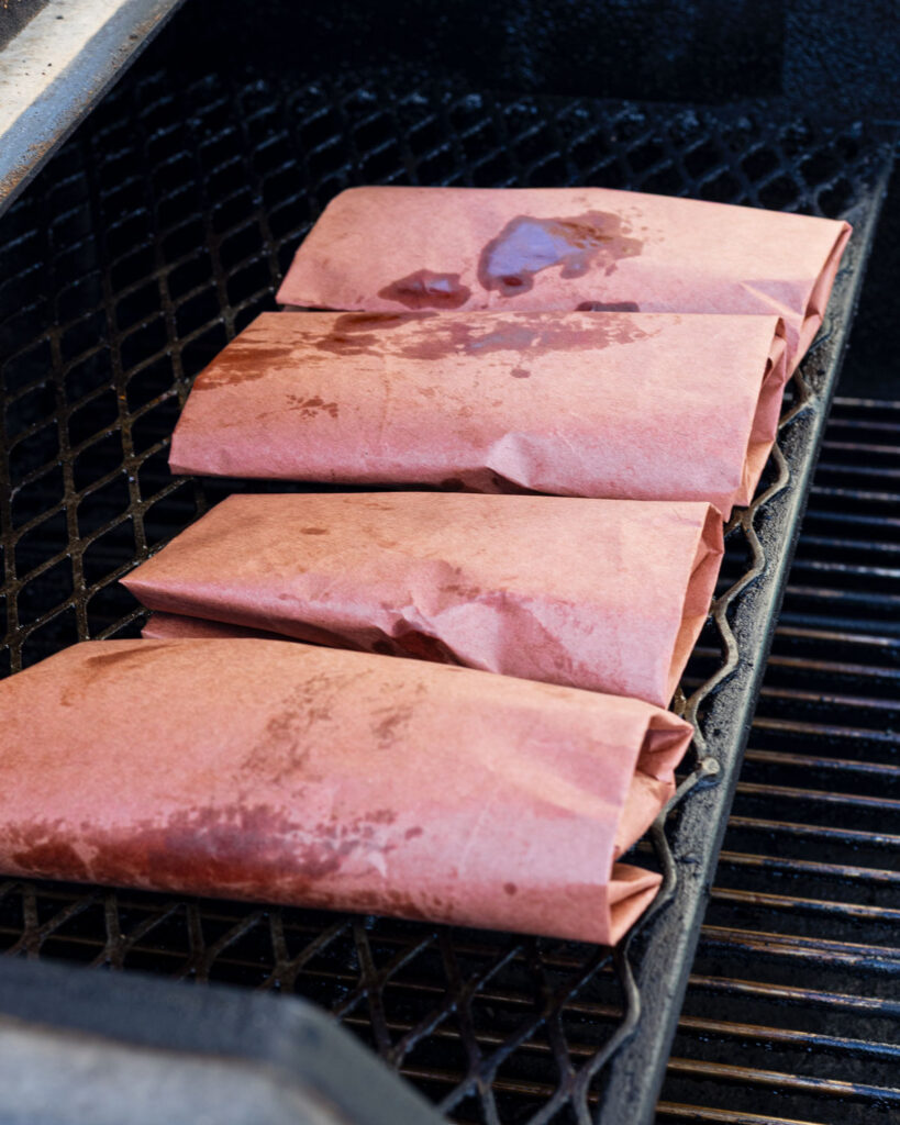 Four butcher paper wrapped chicken breasts on smoker grates finishing at 250°F