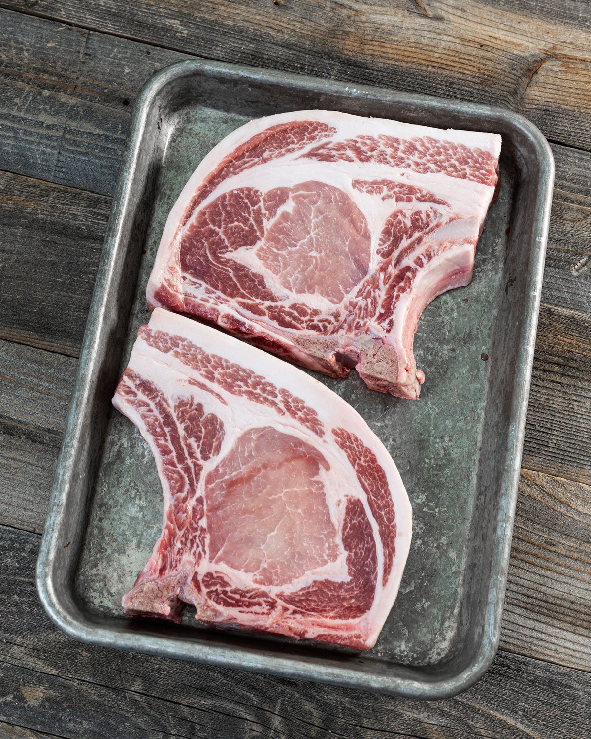 Two raw bone-in pork chops on a sheet pan.