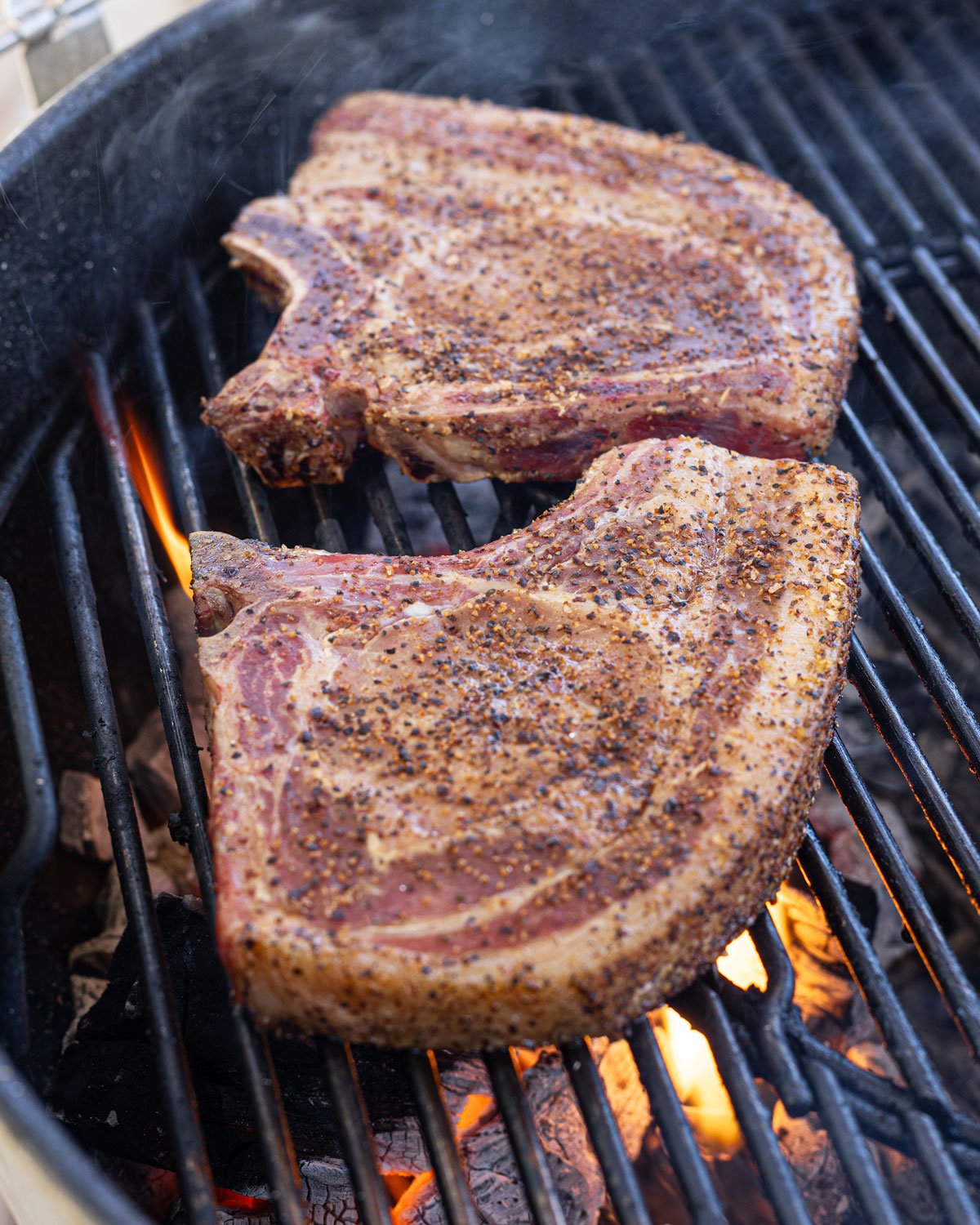 Two bone-in pork chops moved to direct heat to sear on the grill.