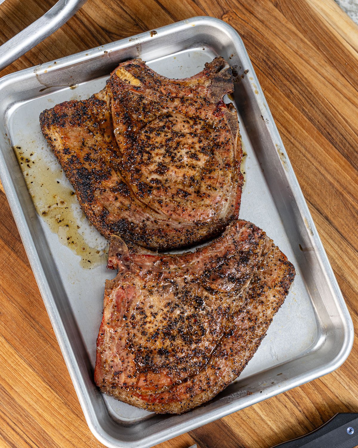 Smoked bone-in pork chops on a sheet pan to rest before serving.