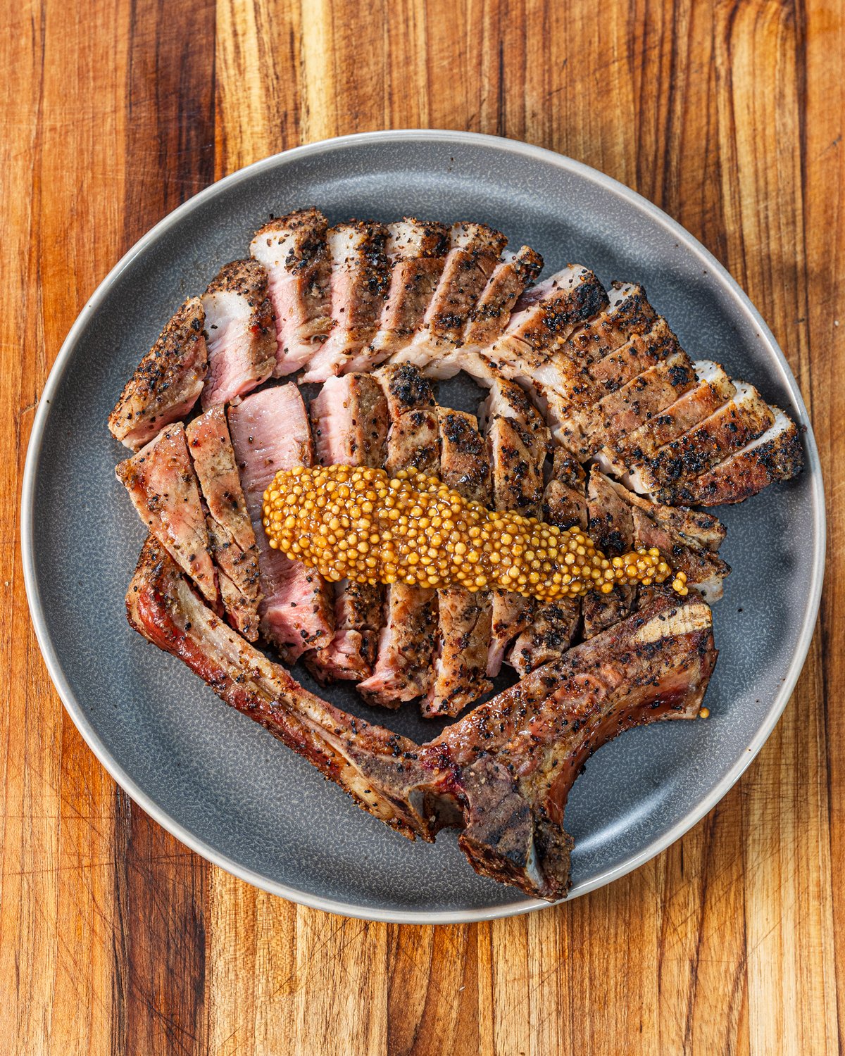 Sliced smoked pork chop on a grey plate topped with whole grain mustard.