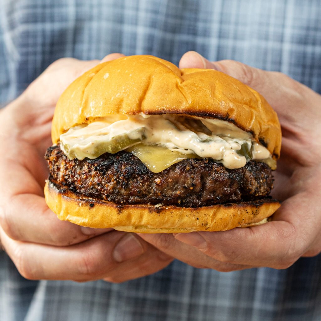 Charcoal grilled burger with pickles, cheese, and cowboy sauce