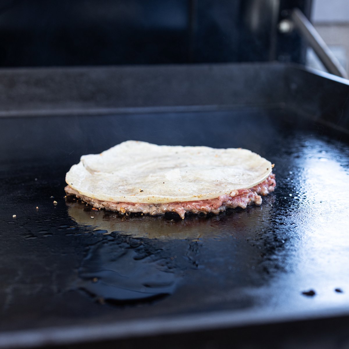 Smashed burger taco is searing on the griddle