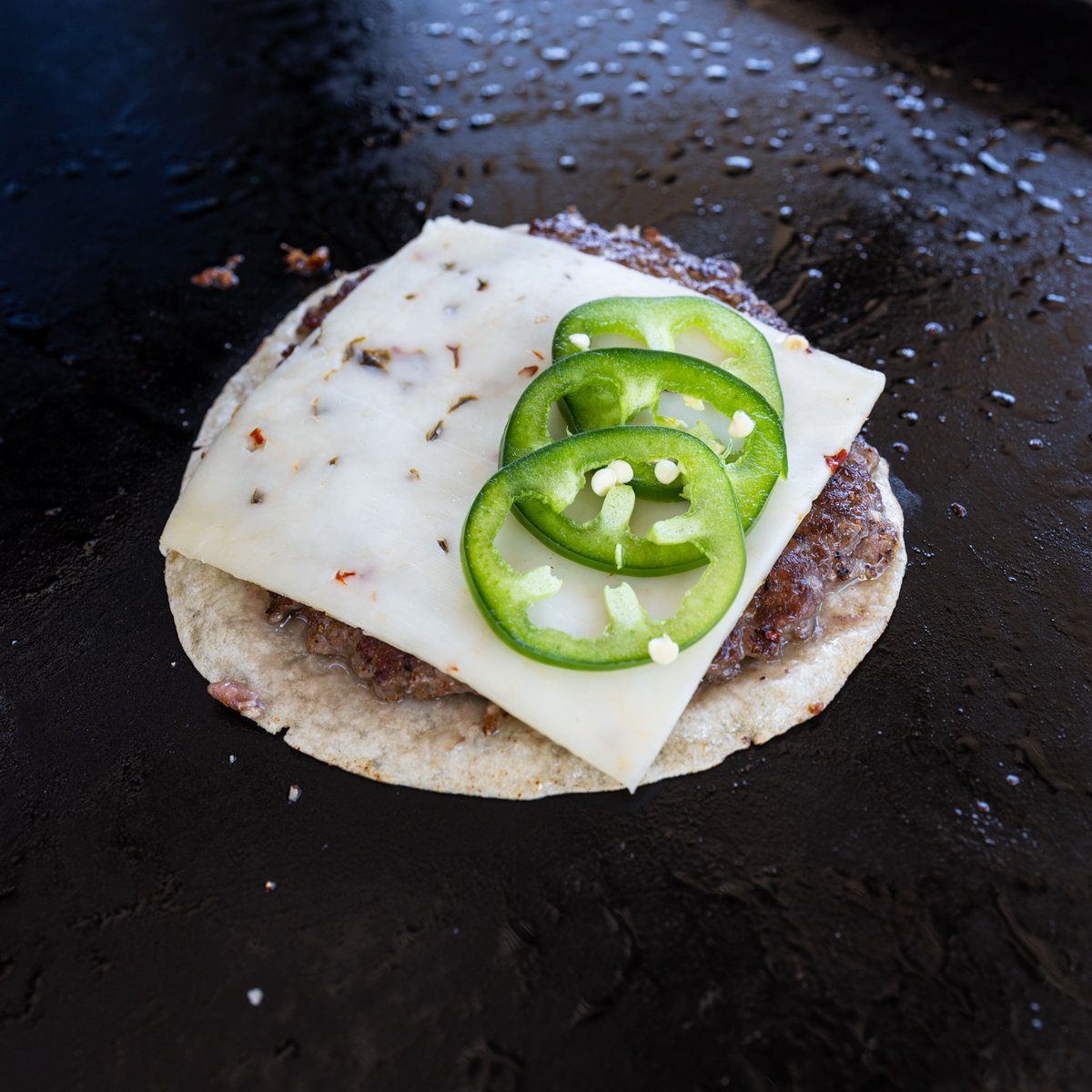 Smashed burger taco topped with cheese and jalapenos on the griddle
