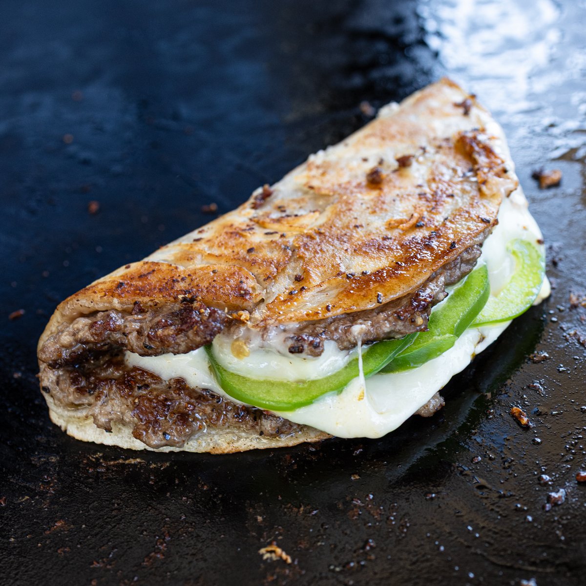 Fried smash burger taco is folded and cooking on the griddle