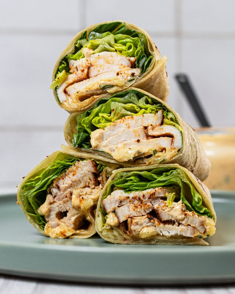 Side view of grilled chicken wraps stacked on a plate.