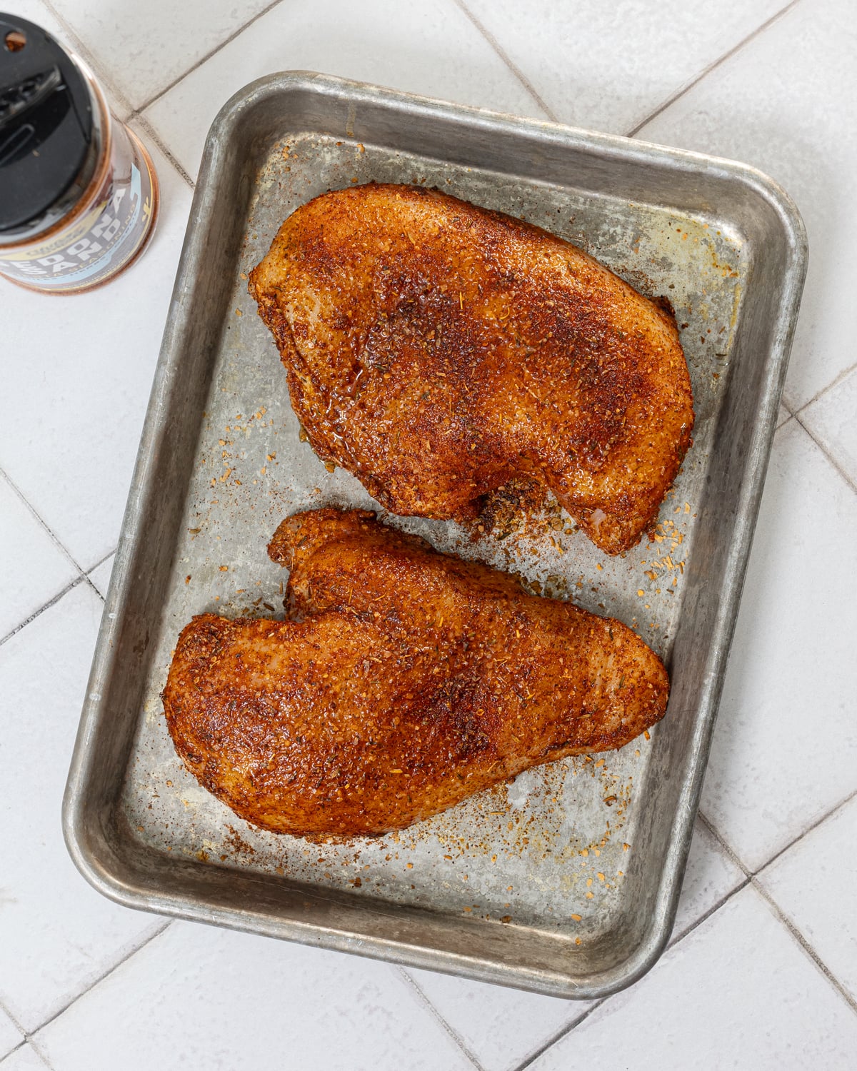 Two chicken breasts heavily coated in Sedona Sand Fiesta Seasoning on a sheet pan, ready for the grill