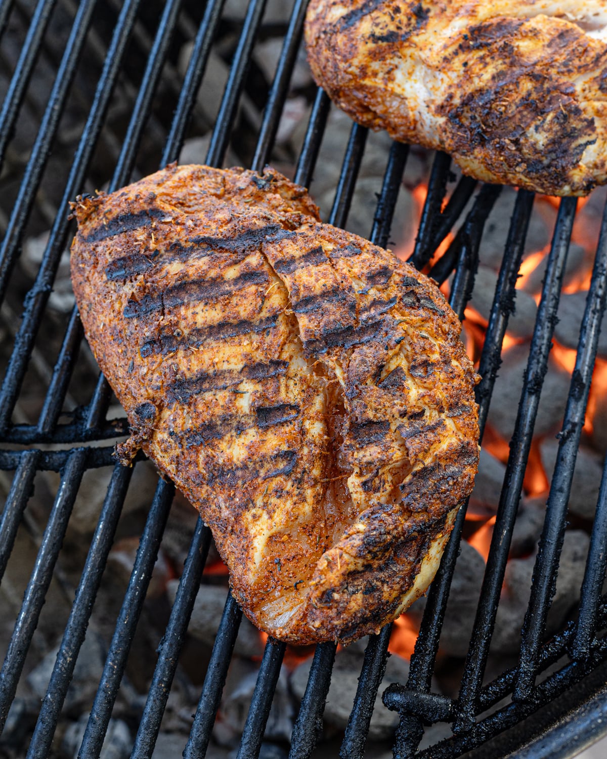 Seasoned chicken breast with defined grill marks searing over live charcoal on a kettle grill