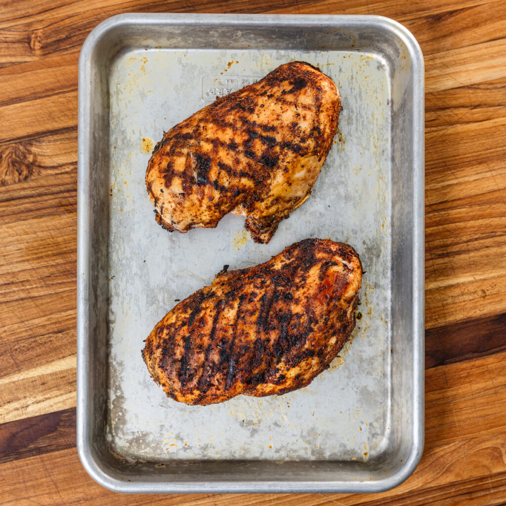 Overhead shot of two grilled chicken breasts on a sheet pan to rest.