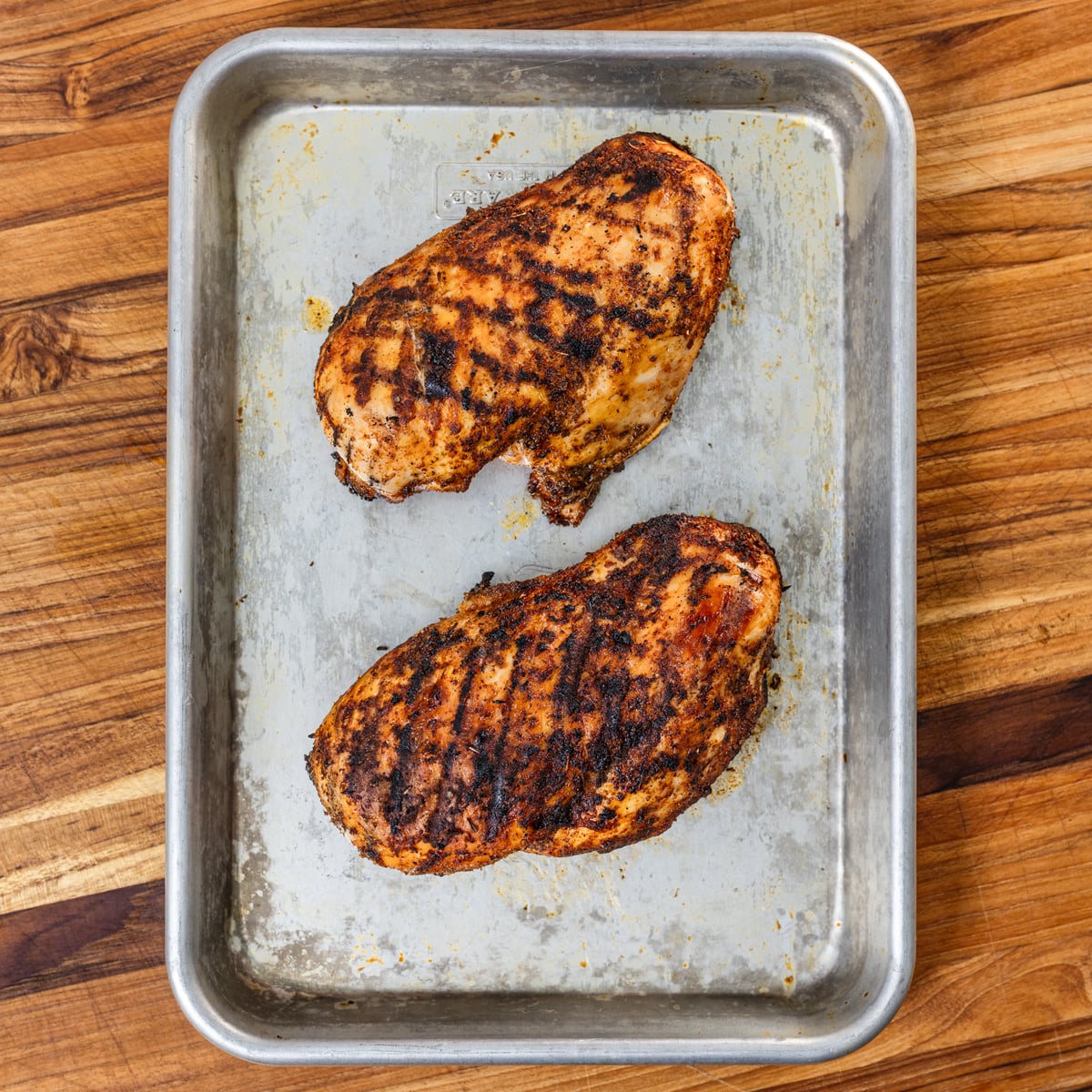 Grilled chicken breast with deep grill marks and seasoned crust resting on the grill grate