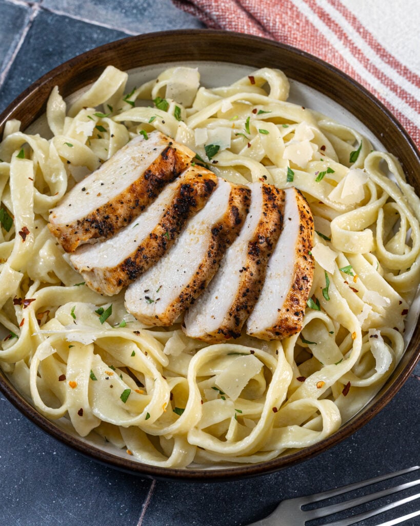 Sliced grilled chicken breast on creamy pasta with Alfredo sauce