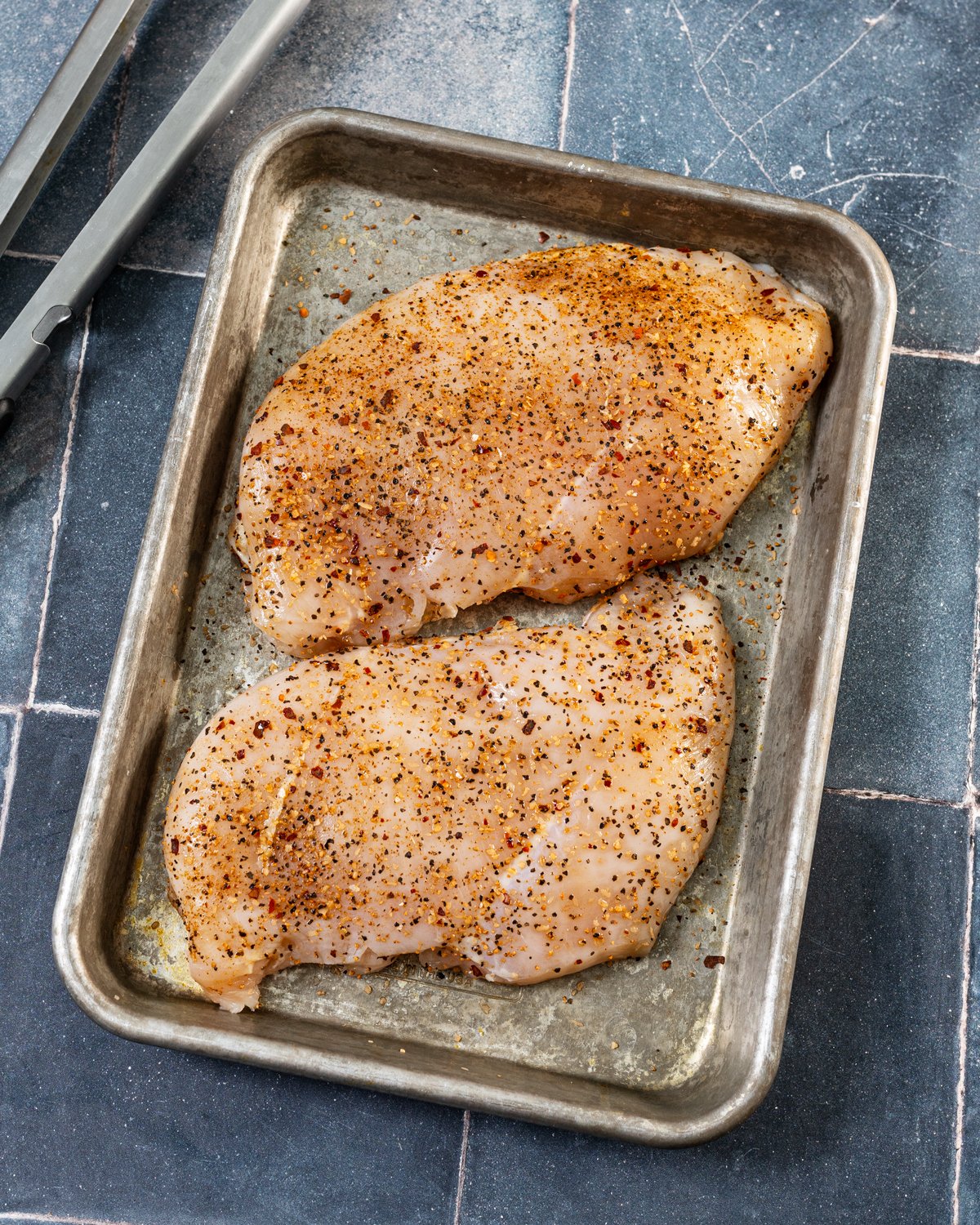 Seasoned chicken breasts flattened on a baking sheet