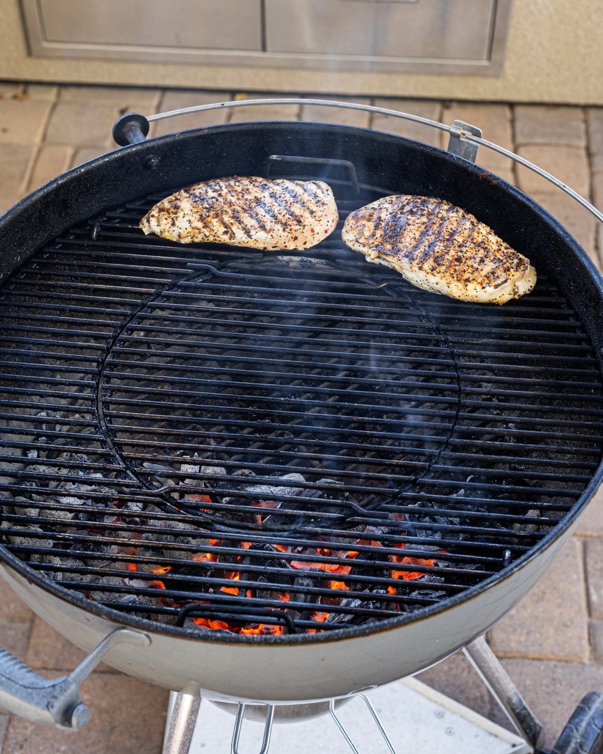 Chicken breast is cooking on the cool side of the charcoal grill