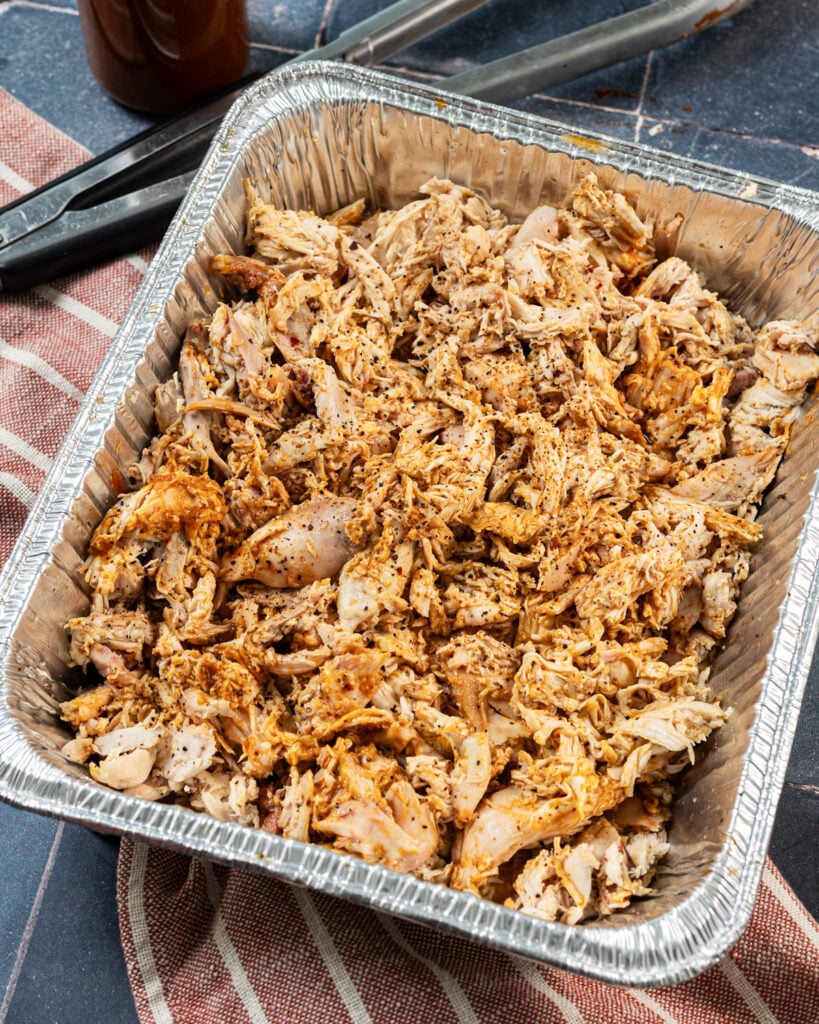 Seasoned and sauced smoked pulled chicken in a foil pan.