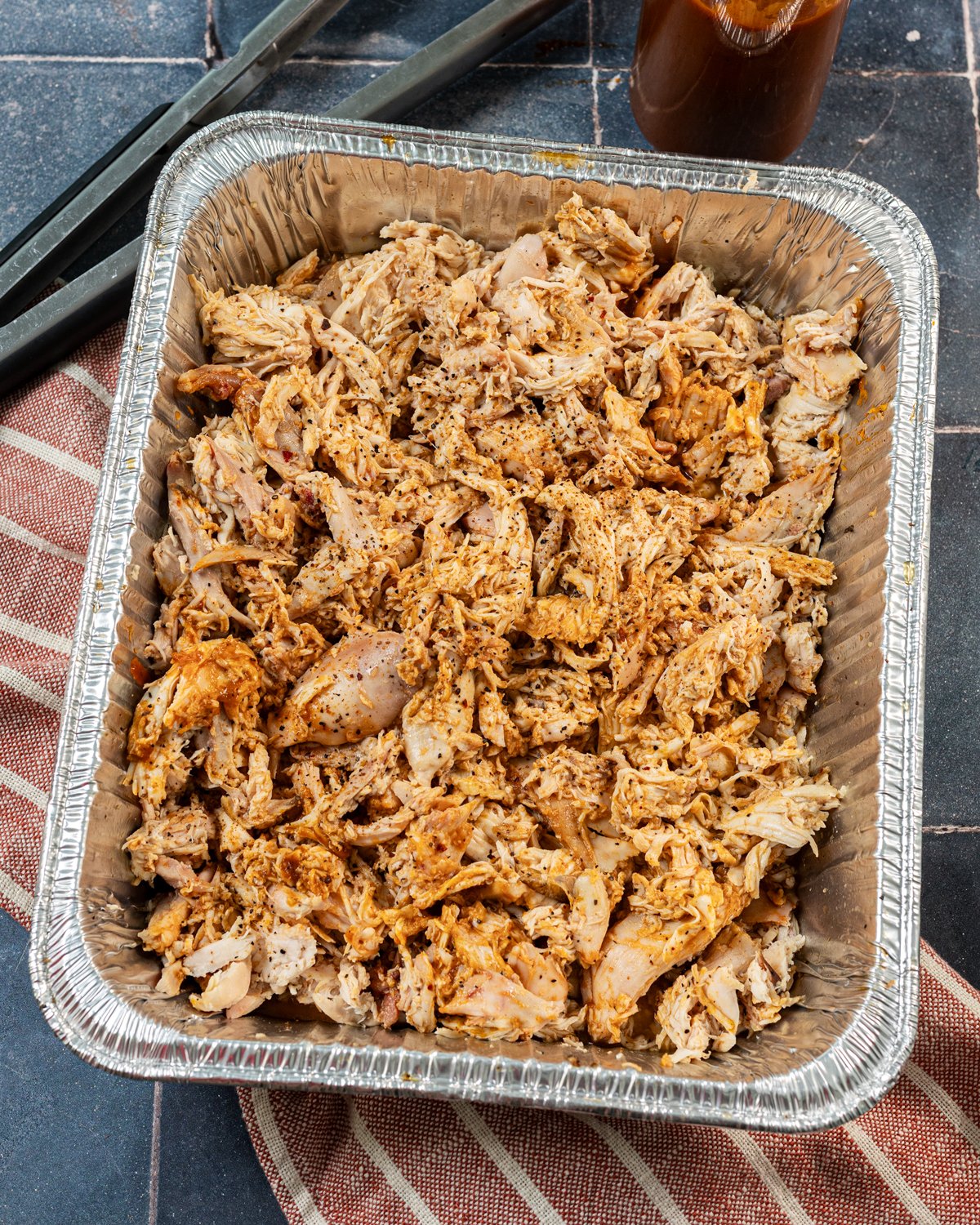Smoked pulled chicken in a foil pan with sauce and seasoning.