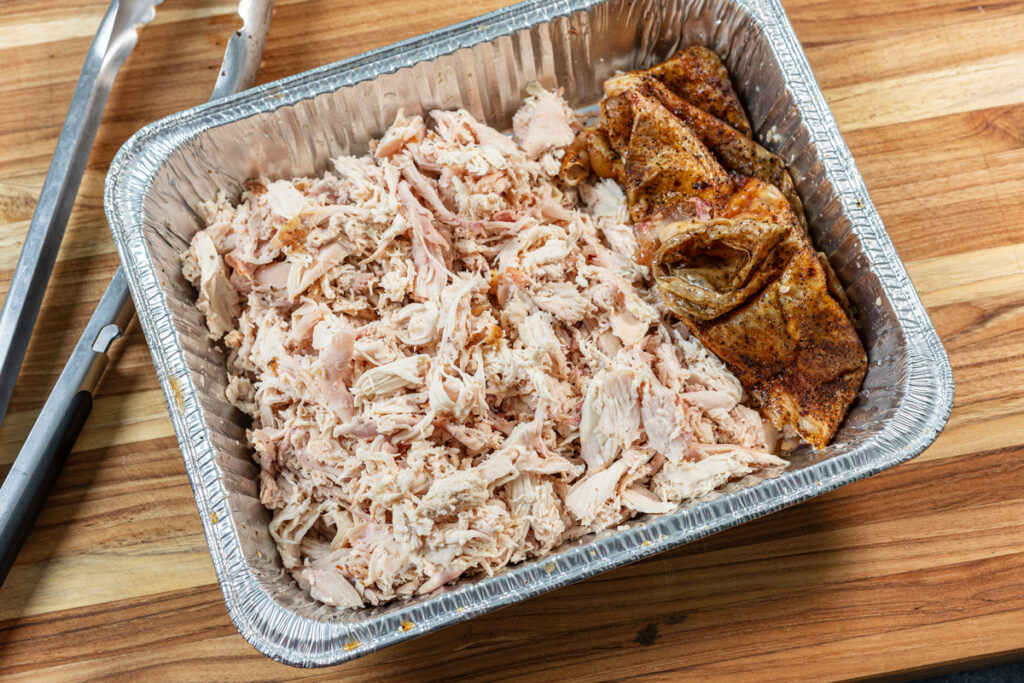 Smoked chicken shredded in a pan with the crispy smoked skin set aside
