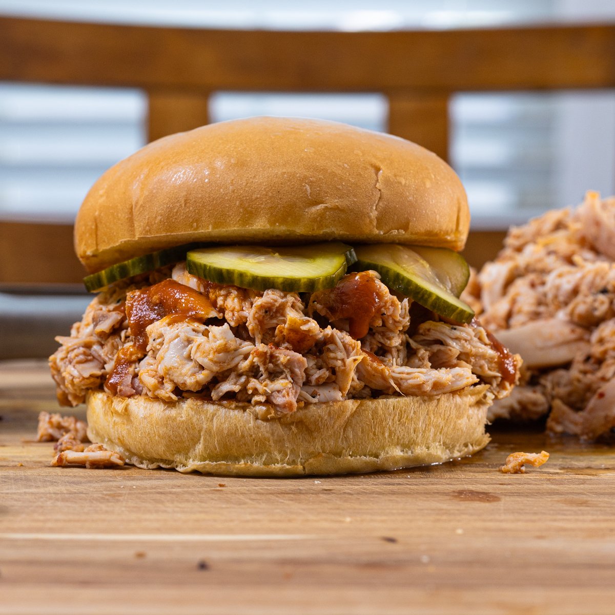 Smoked pulled chicken sandwich with pickles and sauce.