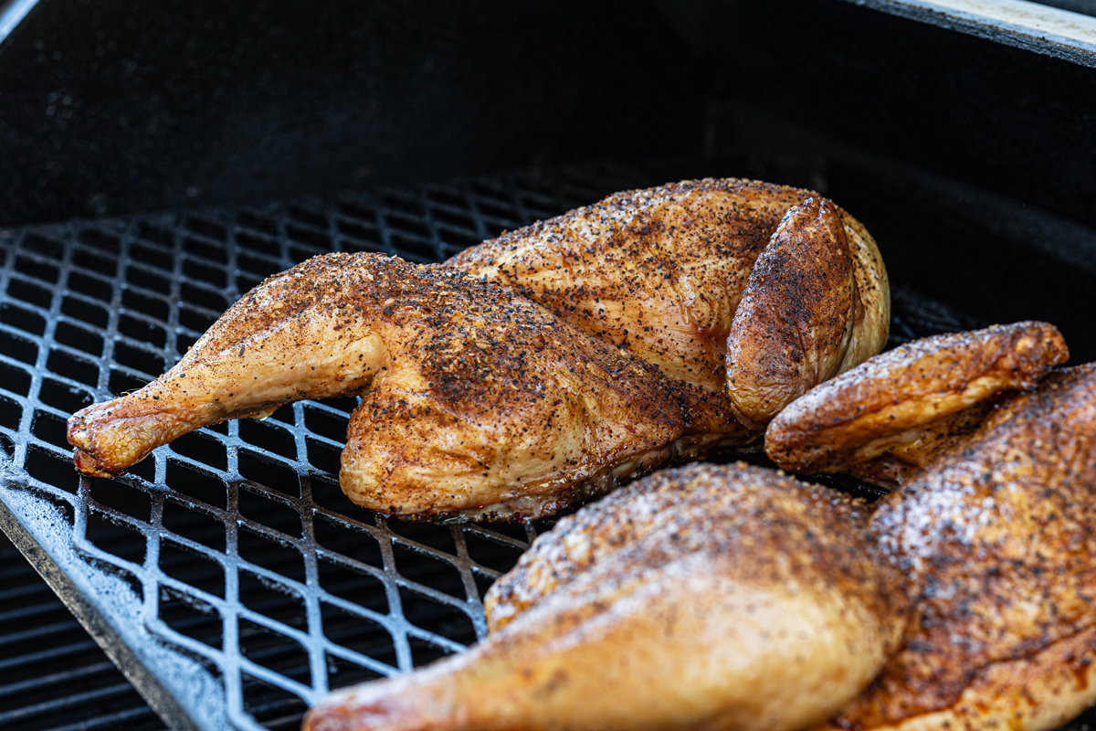 Smoked chicken halves with deep golden brown skin, nearly done
