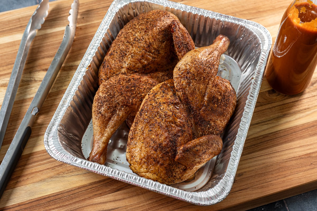 Smoked chicken halves in a foil pan.