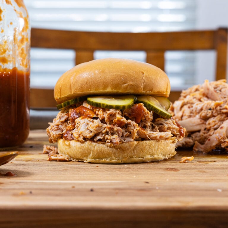 Side view of a smoked pulled chicken sandwich on a wooden board.