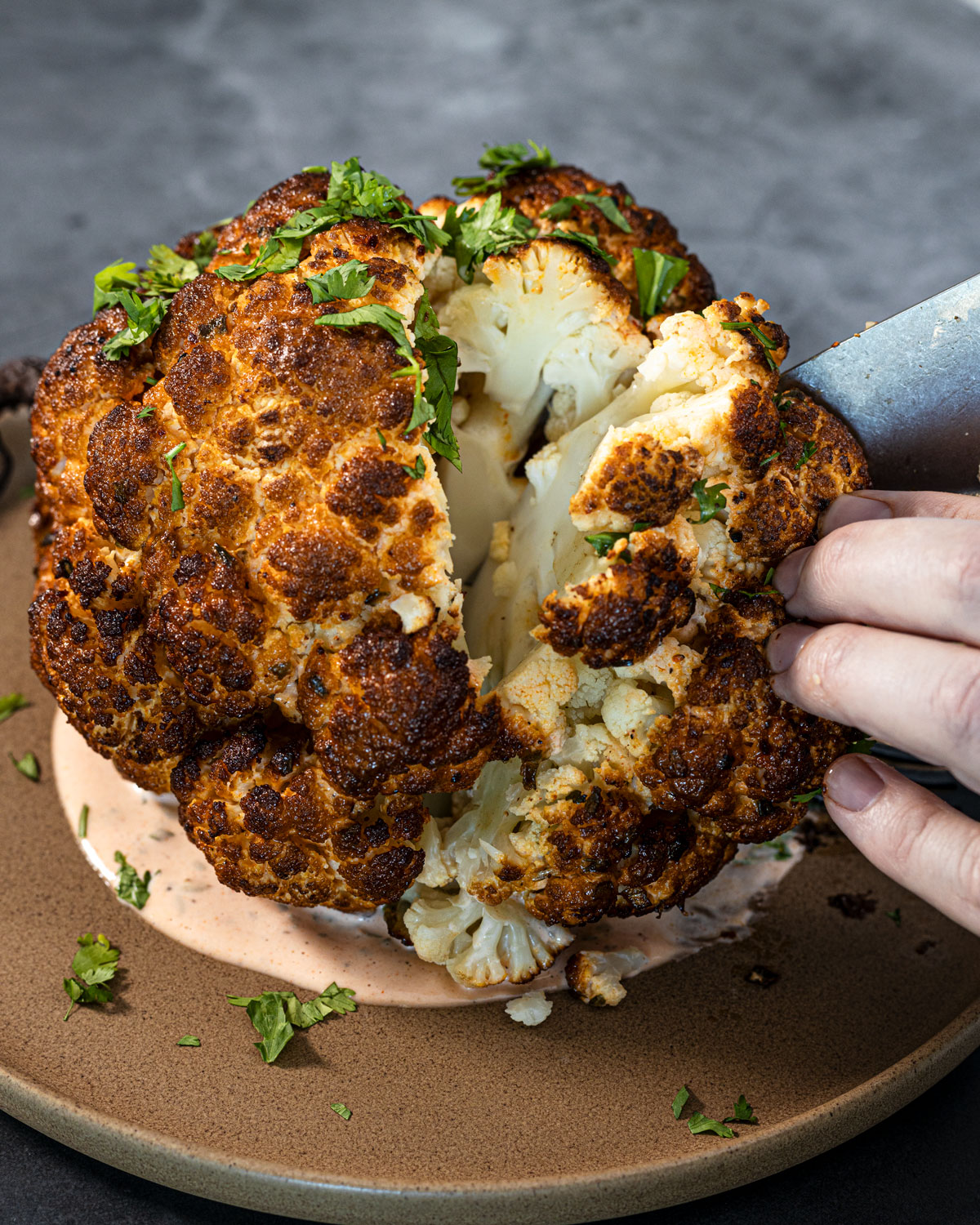 Slicing into a smoked whole cauliflower on a plate with buffalo mayo
