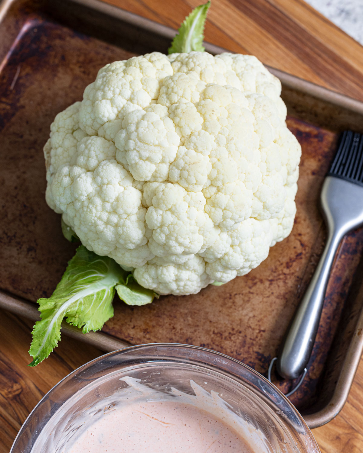 Steamed cauliflower is on a baking sheet next to buffalo mayo