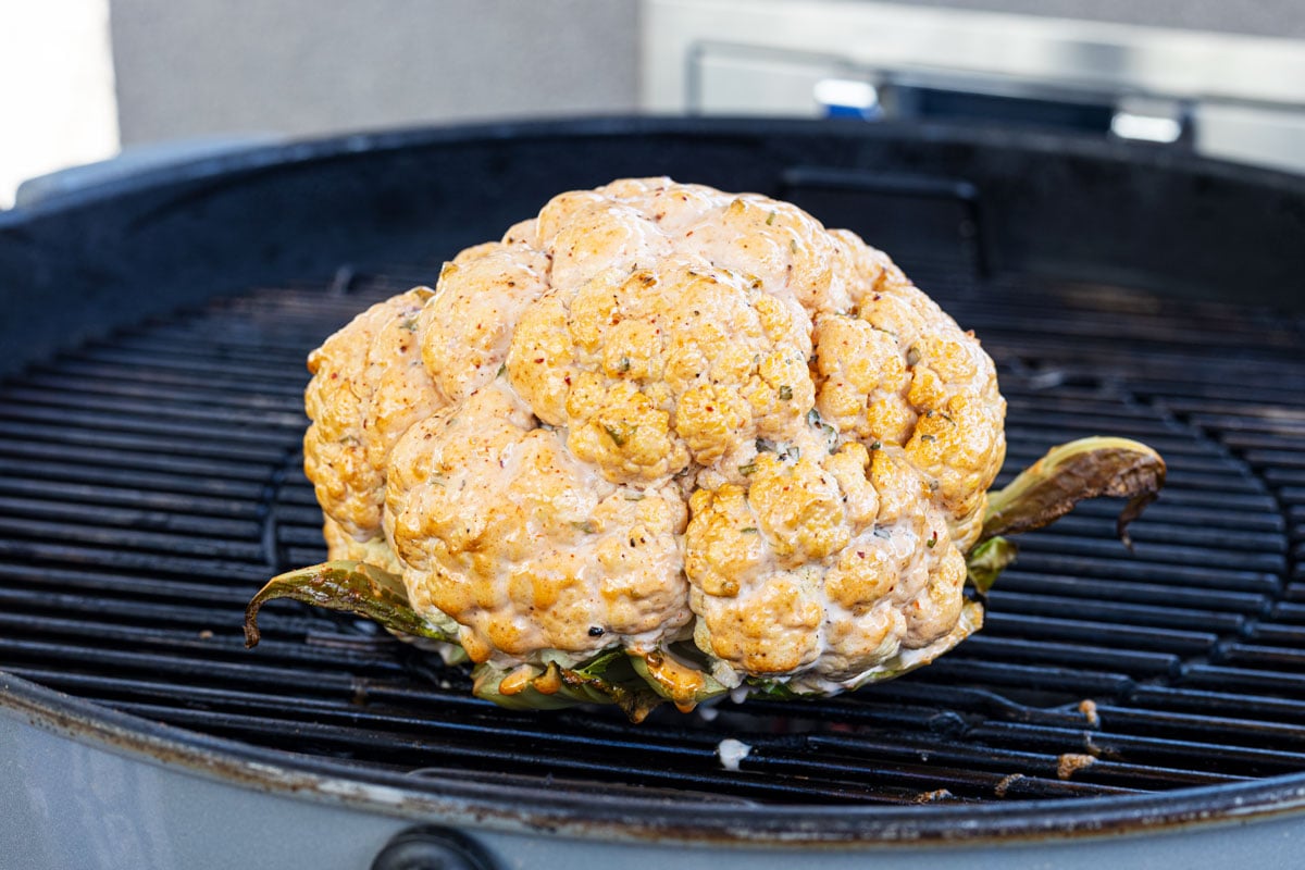 The marinated cauliflower is cooking indirectly on a charcoal grill
