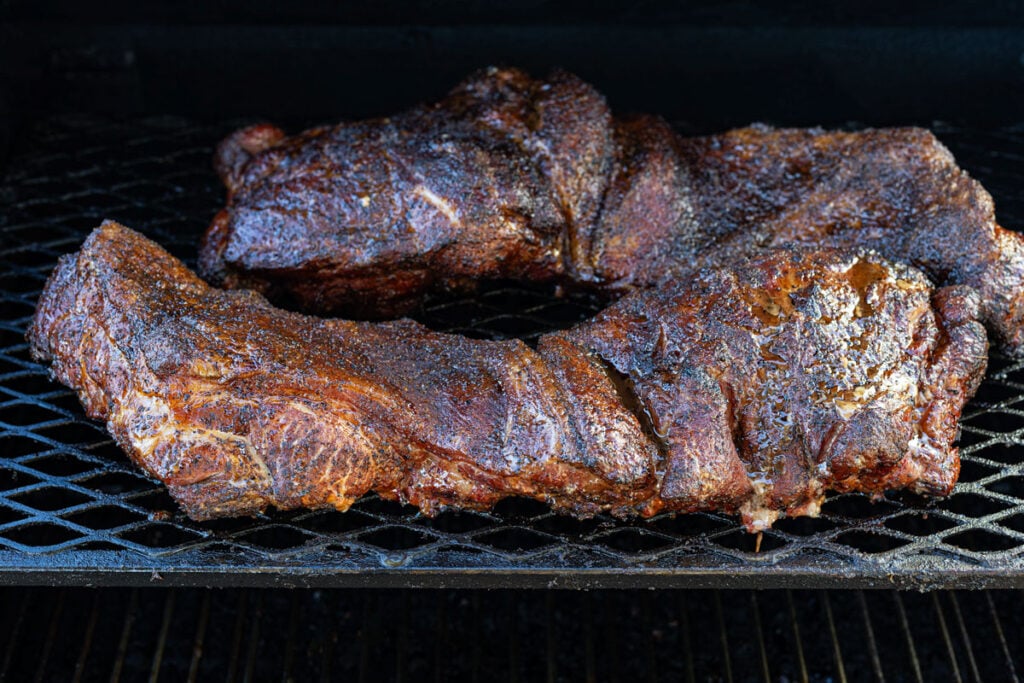 Smoked butterflied pork butt laid flat on smoker grates showing even surface exposure