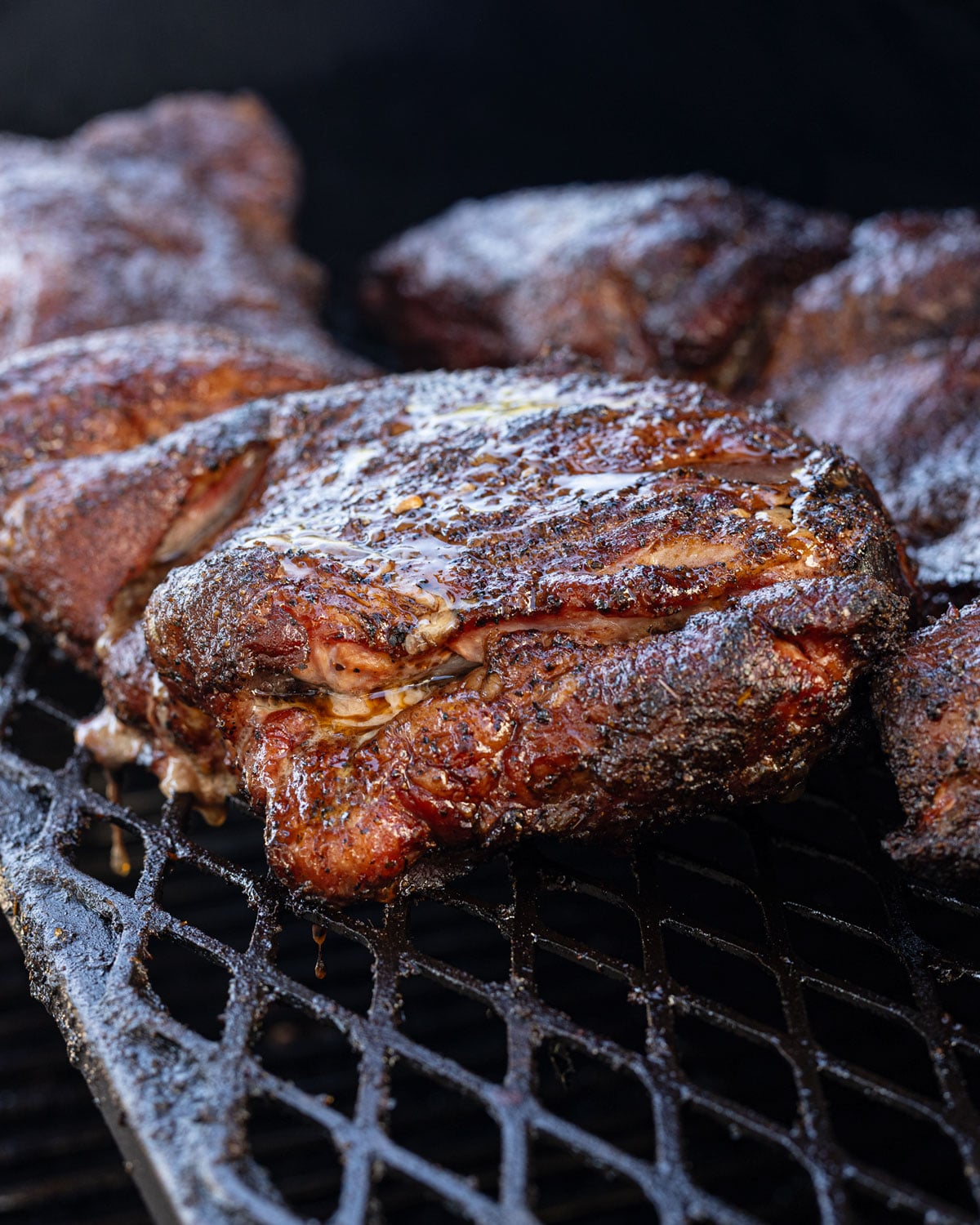 Close up of bark and rendering fat on a butterflied pork butt mid cook on the smoker grates