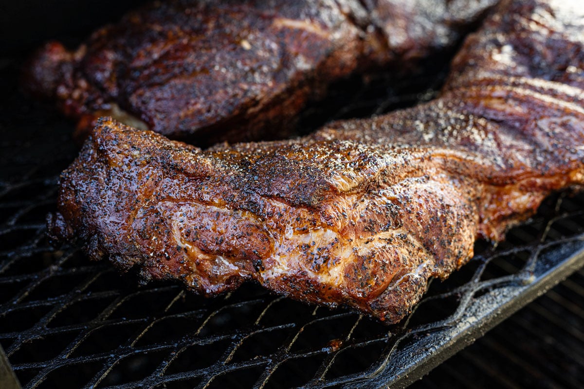 Close up of dark bark forming on butterflied pork butt mid cook on the smoker