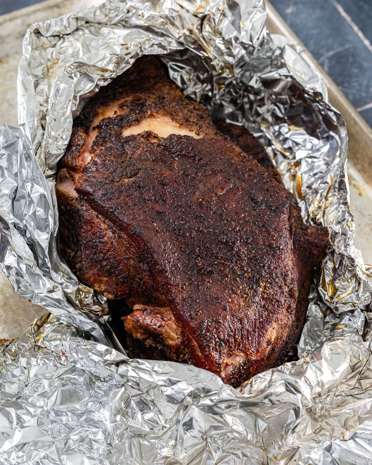 Smoked pork butt unwrapped from foil after resting showing dark set bark and rendered juices