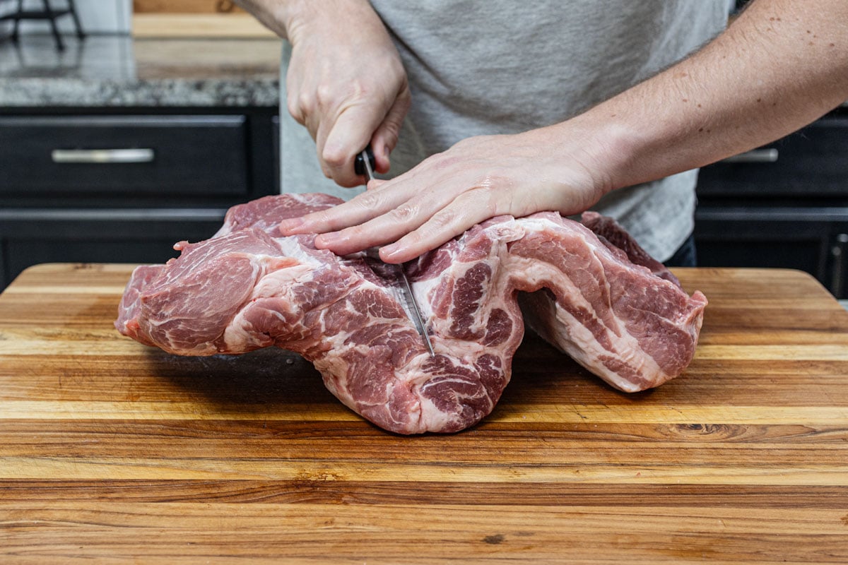 Boneless pork butt butterflied open flat on a wood cutting board showing muscle seams