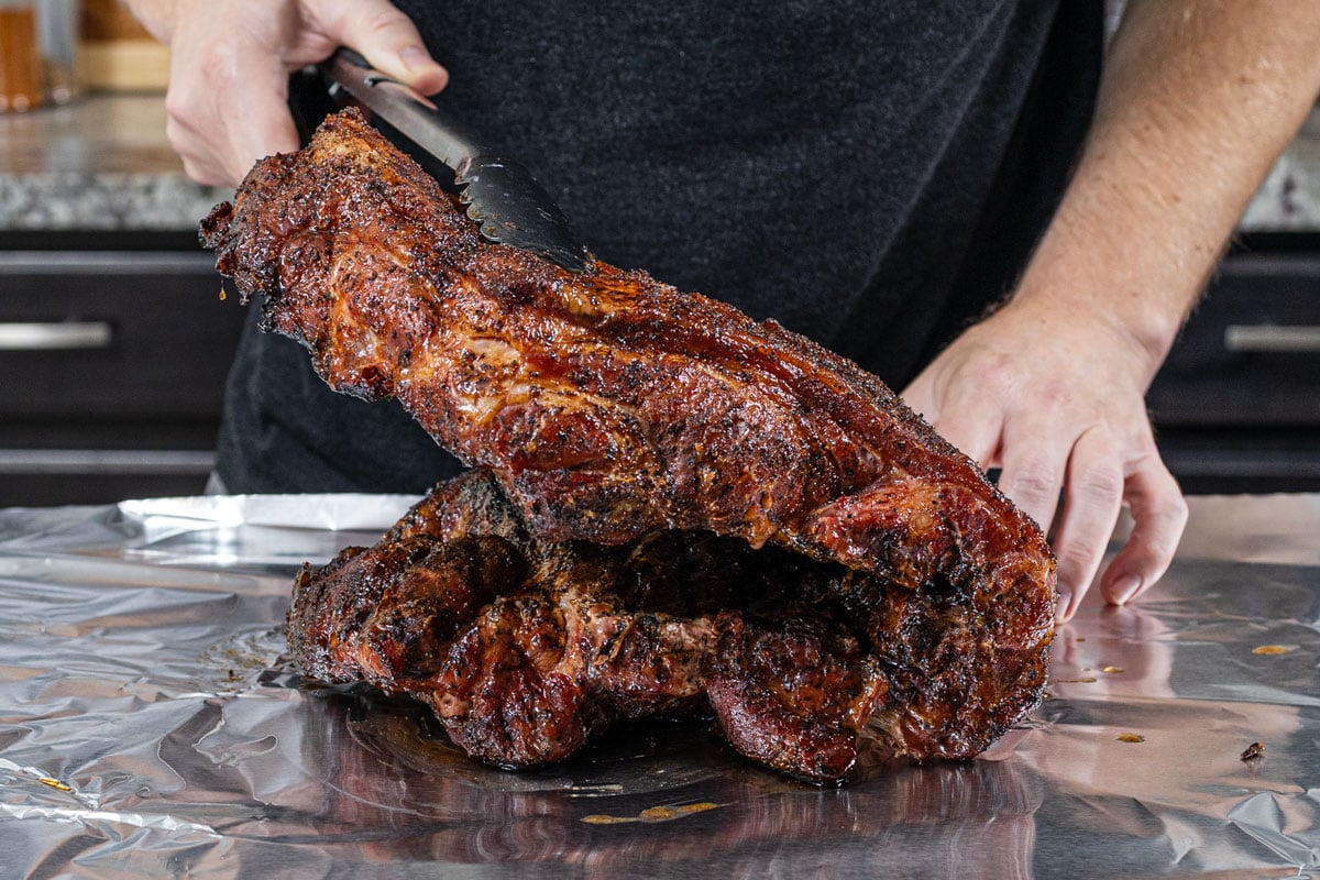Smoked butterflied pork butt being folded back in on itself before wrapping in foil