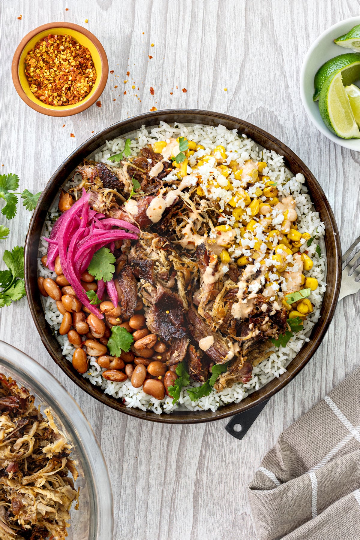 Smoked carnitas burrito bowl overhead with charred corn, pickled red onions, pinto beans, chipotle lime crema, and cotija on cilantro lime rice