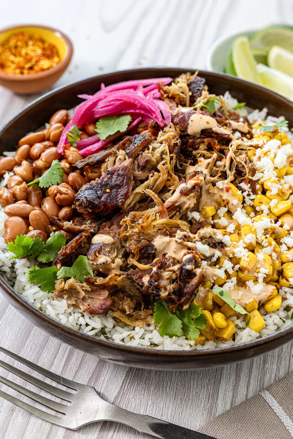 Smoked carnitas burrito bowl angled close up showing caramelized carnitas, charred corn, and chipotle lime crema drizzle
