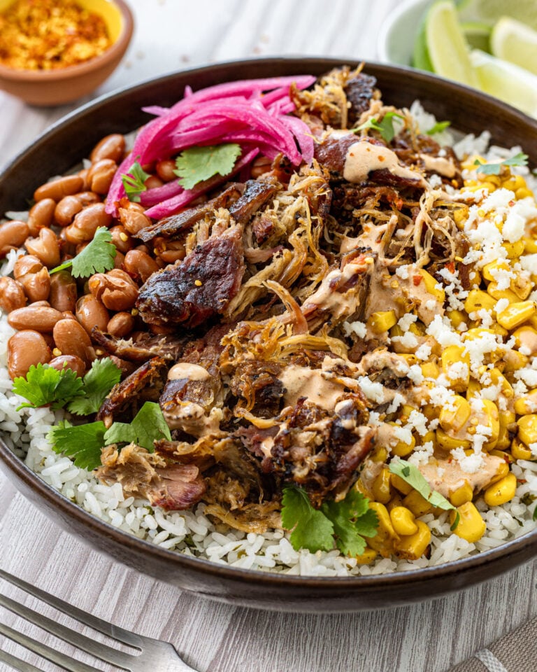 Smoked carnitas burrito bowl angled close up showing caramelized carnitas, charred corn, and chipotle lime crema drizzle