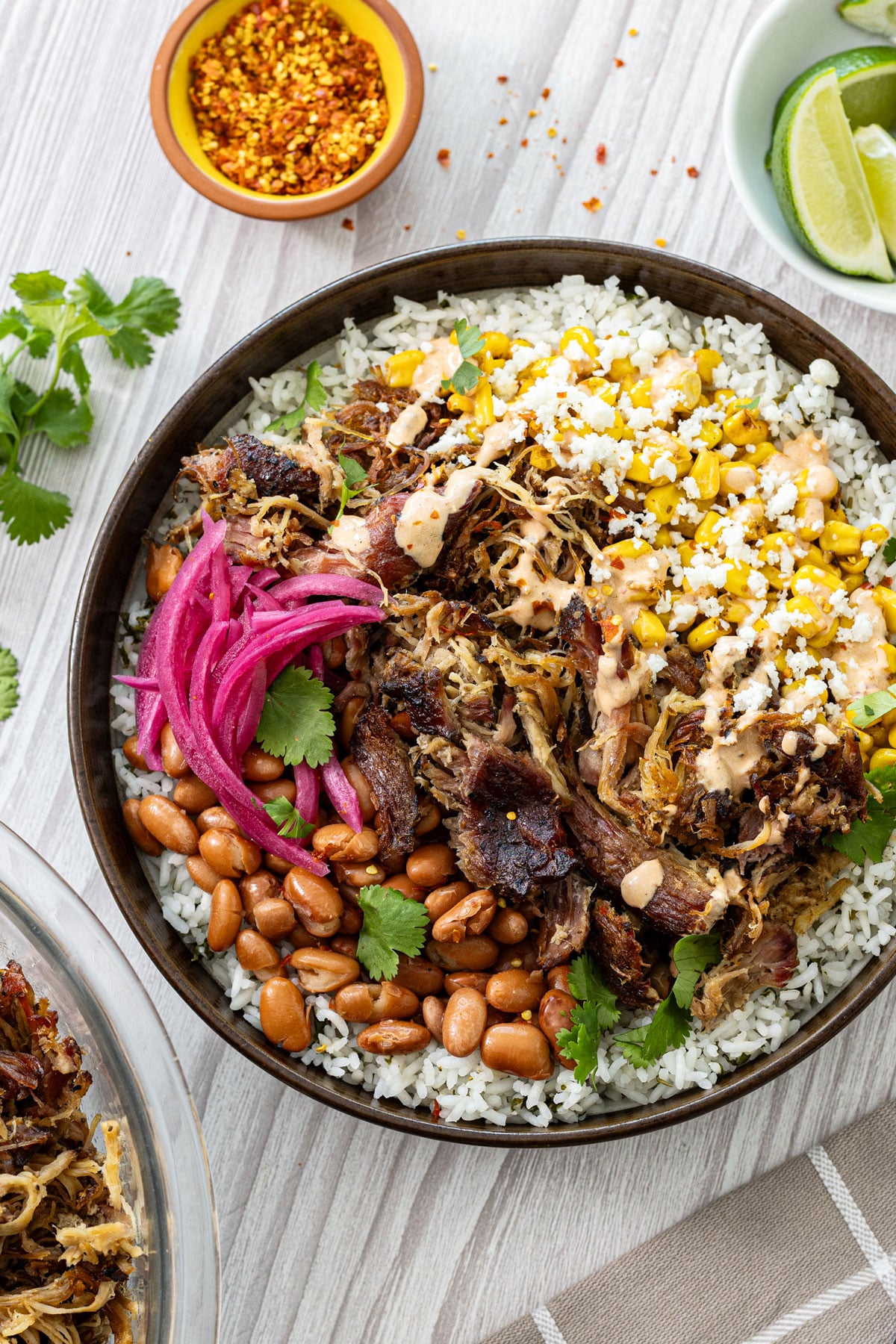 Smoked carnitas burrito bowl overhead portrait with bright pickled red onions, charred skillet corn, and cotija crumble