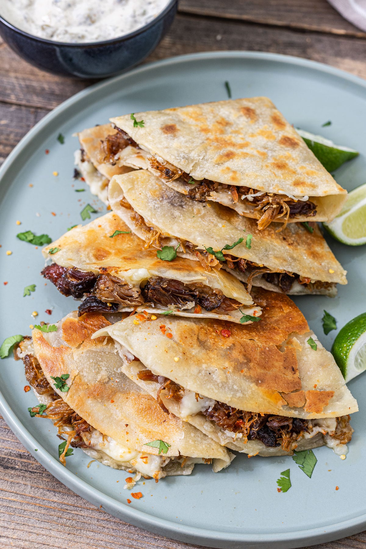 Smoked carnitas quesadilla stacked wedges showing caramelized tortilla, Oaxacan cheese, and crisped carnitas with lime and crema