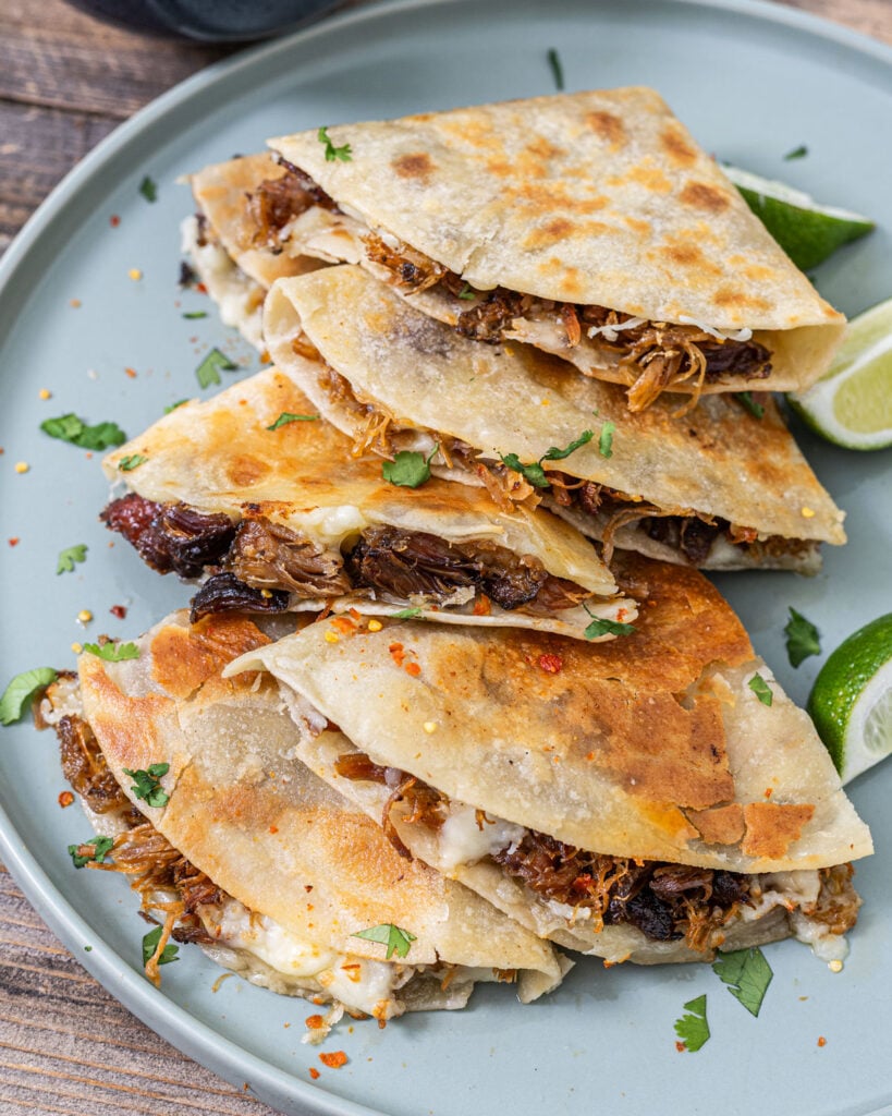 Smoked carnitas quesadilla stacked wedges showing caramelized tortilla, Oaxacan cheese, and crisped carnitas with lime and crema
