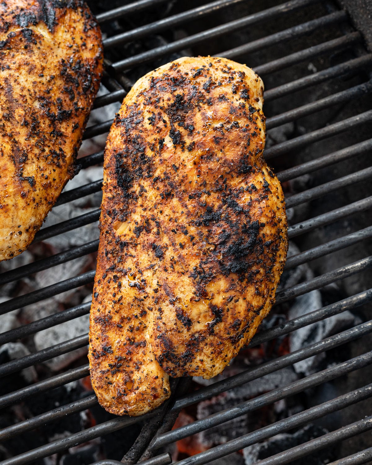 Seasoned chicken breast with a charred crust searing over live charcoal on a kettle grill