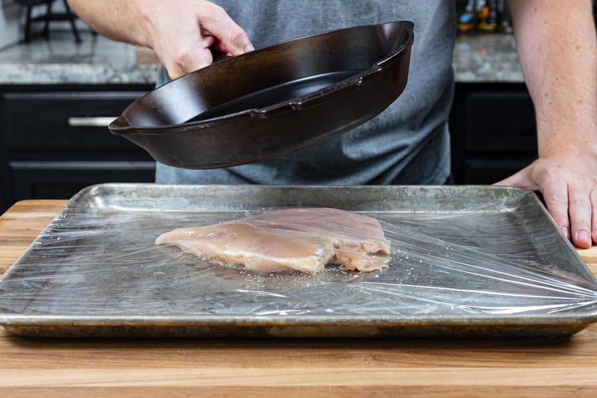 Flattening a chicken breast under a cast iron skillet on a sheet pan before grilling