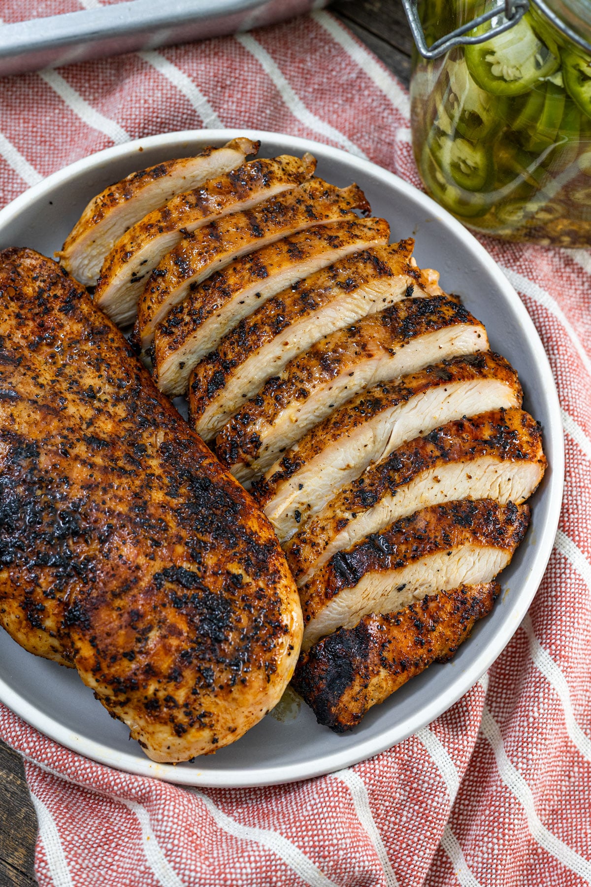 Sliced grilled chicken breast on a plate showing juicy interior with pickled jalapeño jar in the background