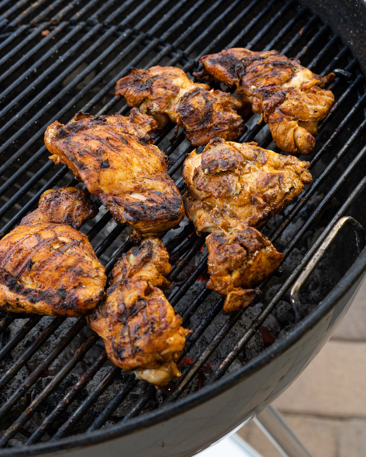 Marinated chicken thighs searing over live charcoal on a kettle grill